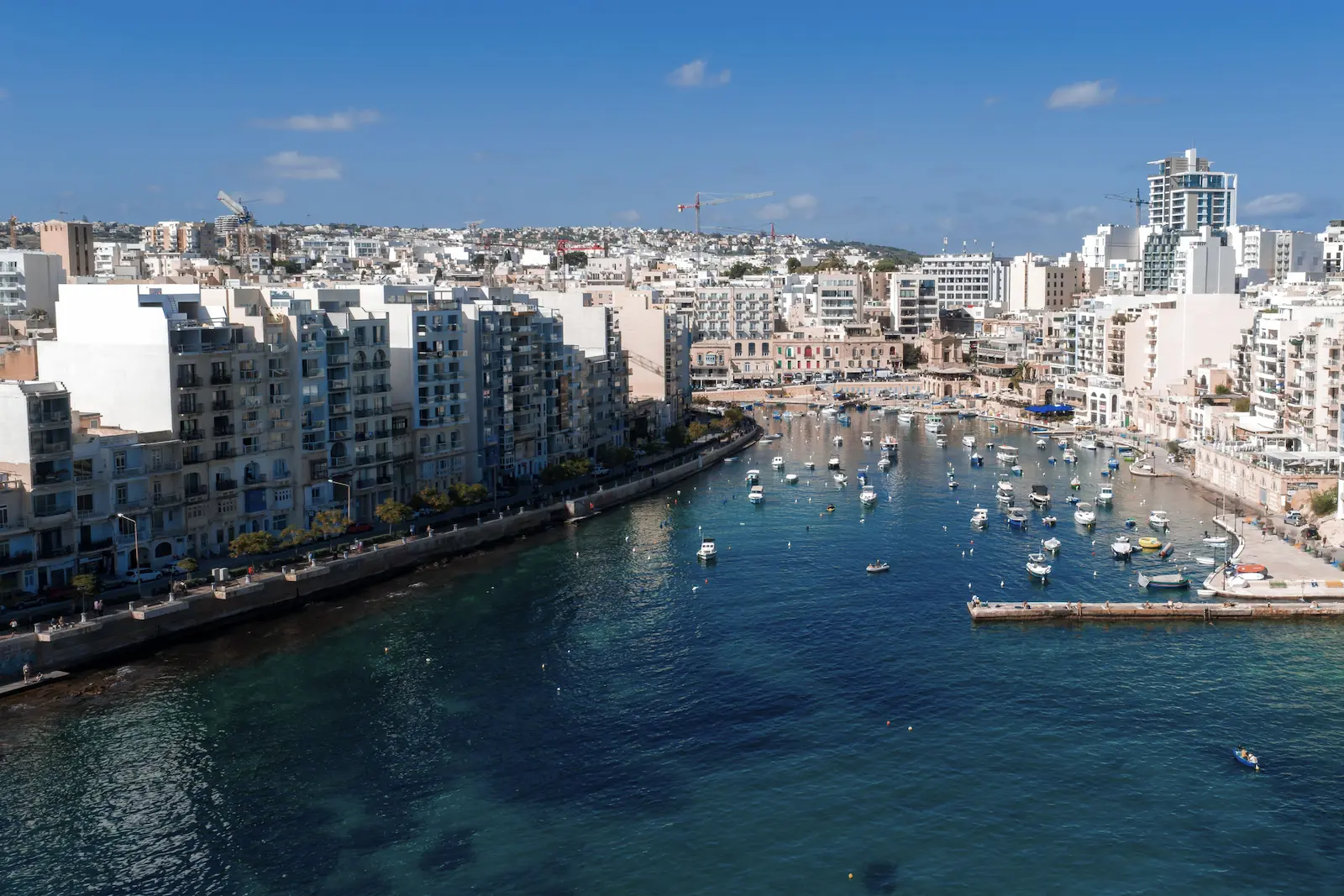 Panoramablick auf die Spinola Bay mit Booten und städtischer Bebauung in St. Julian’s auf Malta.